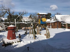 Un espacio exterior cubierto de nieve, con un faro rojo, una estructura de juegos de madera y un pequeño edificio de madera.
