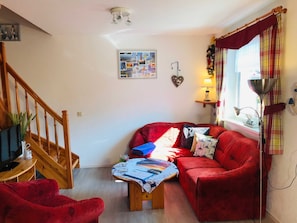 Ein gemütliches Wohnzimmer mit einem roten Sofa, einer Holztreppe, einer Wandleuchte und einem Fenster mit Vorhängen.