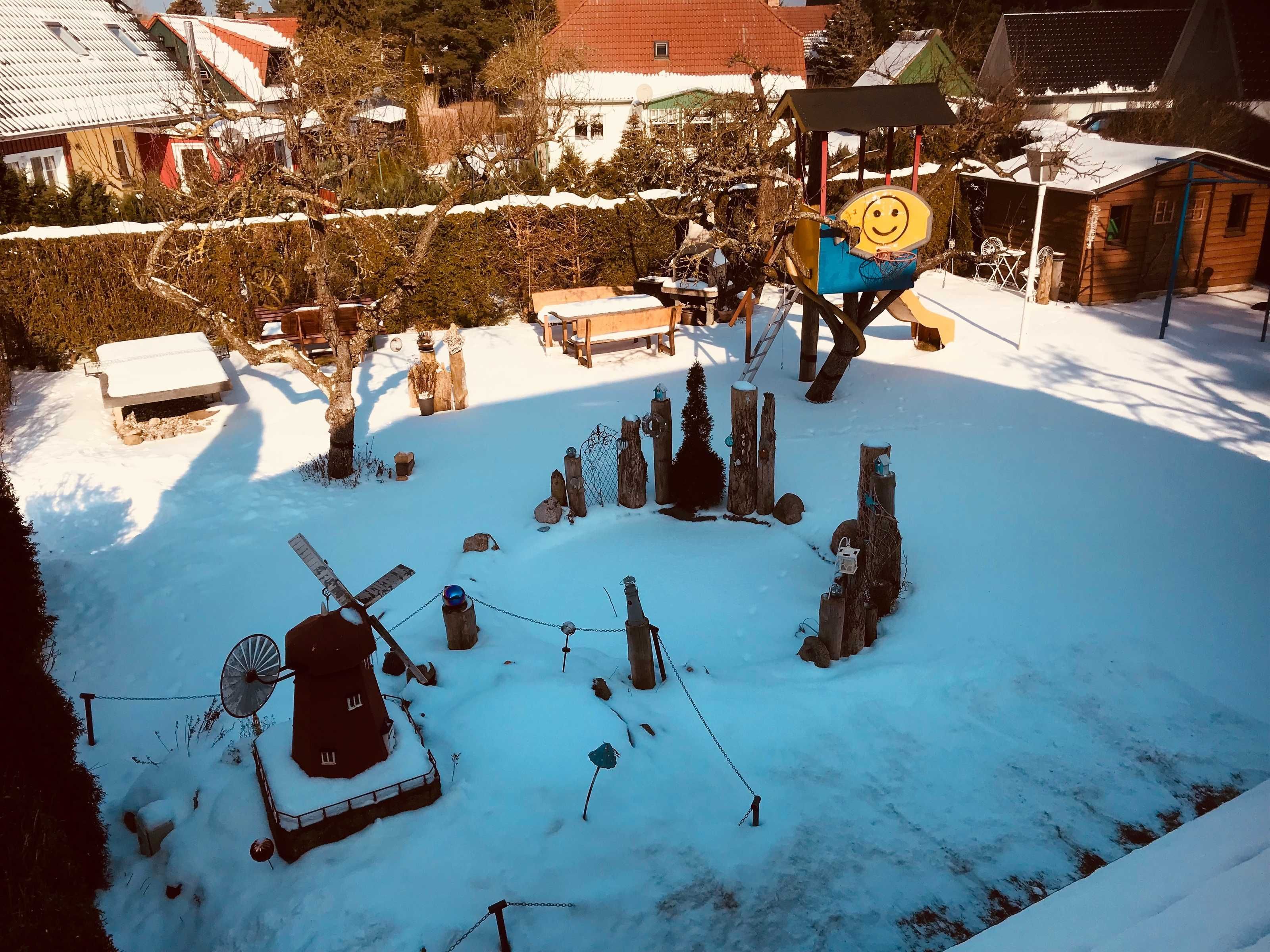 A snow-covered outdoor area with a windmill, wooden structures, and a smiling sun decoration.