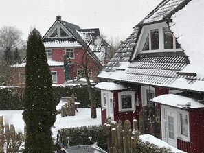 Lumipeitteinen asuinalue, jossa on taloja, puinen aita ja korkea, ikivihreä puu.