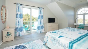 Ein Schlafzimmer mit Bett, Schreibtisch, Fernseher und einem Balkon mit Vorhängen.
