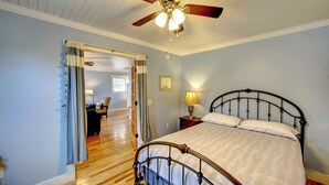 Une chambre à coucher comprenant un lit, une table de chevet, un ventilateur de plafond et une porte donnant sur une autre pièce.