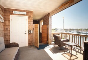 Eine überdachte Veranda mit Korbmöbeln, ein Schild, das einen Bootsanleger kennzeichnet, und ein Blick auf einen Steg sowie Gebäude in der Ferne.