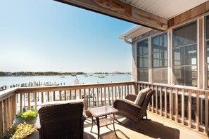 A balcony with wicker furniture, a small table, and a view of the water with boats.
