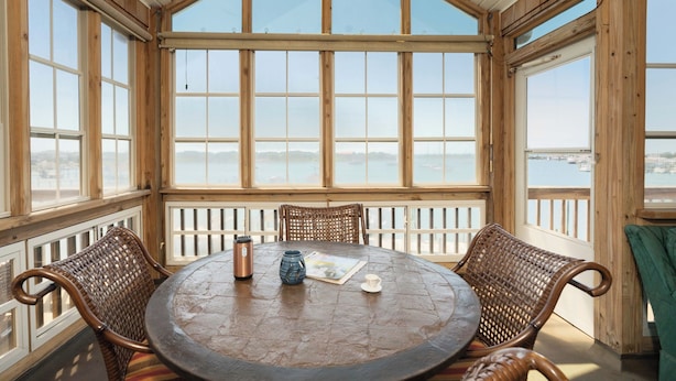 Habitación con paneles de madera, un ventanal grande con vista a un cuerpo de agua, una mesa redonda con sillas y una vista de tierra distante.