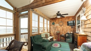 Una habitación acogedora con un sofá verde, un sillón de mimbre, un televisor y vistas al agua.