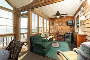 A cozy room with a green sofa, a wicker chair, a television, and a view of the water.