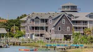 Una casa grande de madera de varios pisos con una torre destacada, varios balcones y un muelle con canoas.