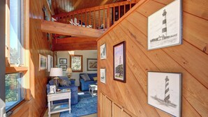 Ein gemütliches Blockhaus-Interieur mit Holzwänden, einem Schlafzimmer im oberen Bereich mit einer Holztreppe, einer Wohnbereich mit blauen Möbeln und mehreren gerahmten Bildern an den Wänden.