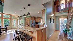 A spacious kitchen with a central island, wooden bar stools, and a dining area with large windows.