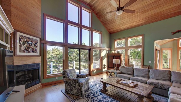A spacious living room with a fireplace, large windows, a ceiling fan, and a view of the outdoors.