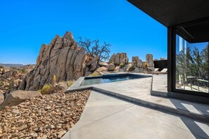 A modern outdoor pool area with a view of rocky terrain and a clear blue sky. - Black Desert House ft in Architectural Digest (Yucca Valley)
