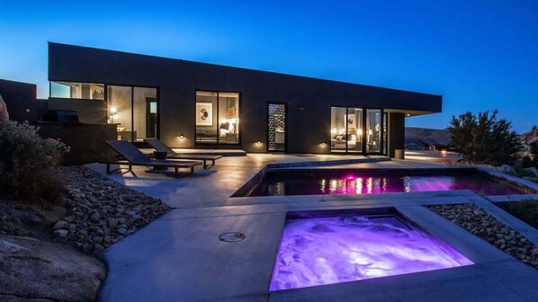 A modern house with a swimming pool, outdoor seating, and a well-lit interior.