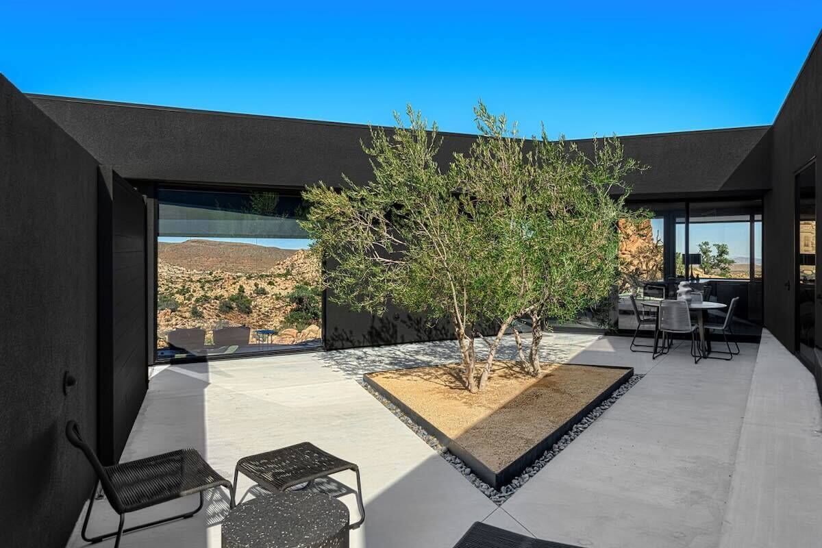 A modern outdoor patio with a seating area, a small tree, and a view of the landscape.