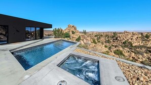 Un espace piscine moderne doté de deux piscines distinctes, une rectangulaire et une carrée, le tout entouré d’un paysage rocheux.