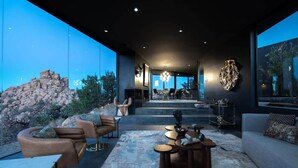 A modern interior with a stone wall, leather furniture, and a large window overlooking a rocky landscape. - Black Desert House ft in Architectural Digest (Yucca Valley)
