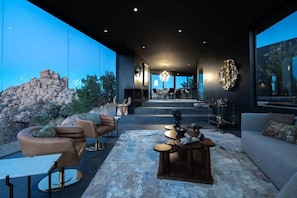 A modern interior with a stone wall, leather furniture, and a large window overlooking a rocky landscape. - Black Desert House ft in Architectural Digest (Yucca Valley)