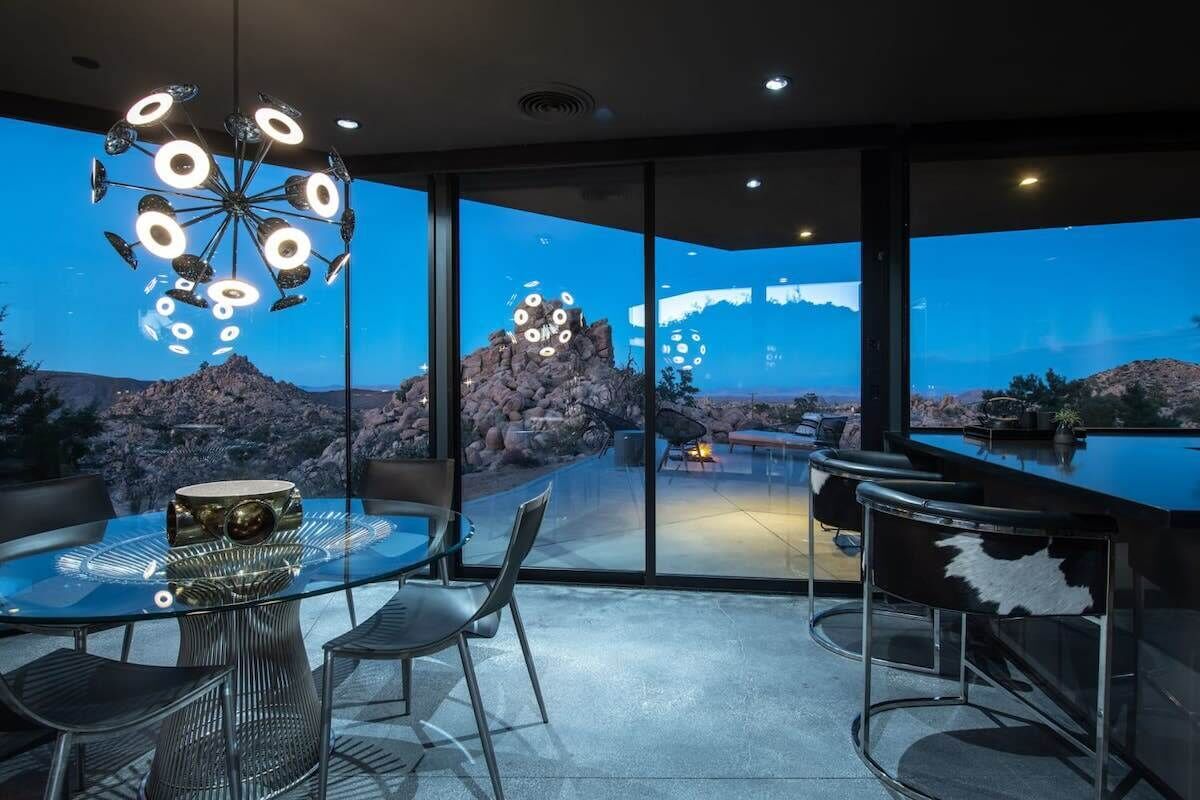 A modern dining area with a glass table, metal chairs, and a unique chandelier.