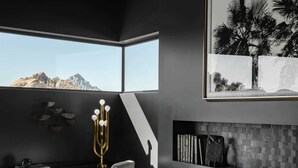 Un salon moderne avec un canapé en cuir, un bureau avec un ordinateur et une grande fenêtre donnant sur un paysage montagneux.