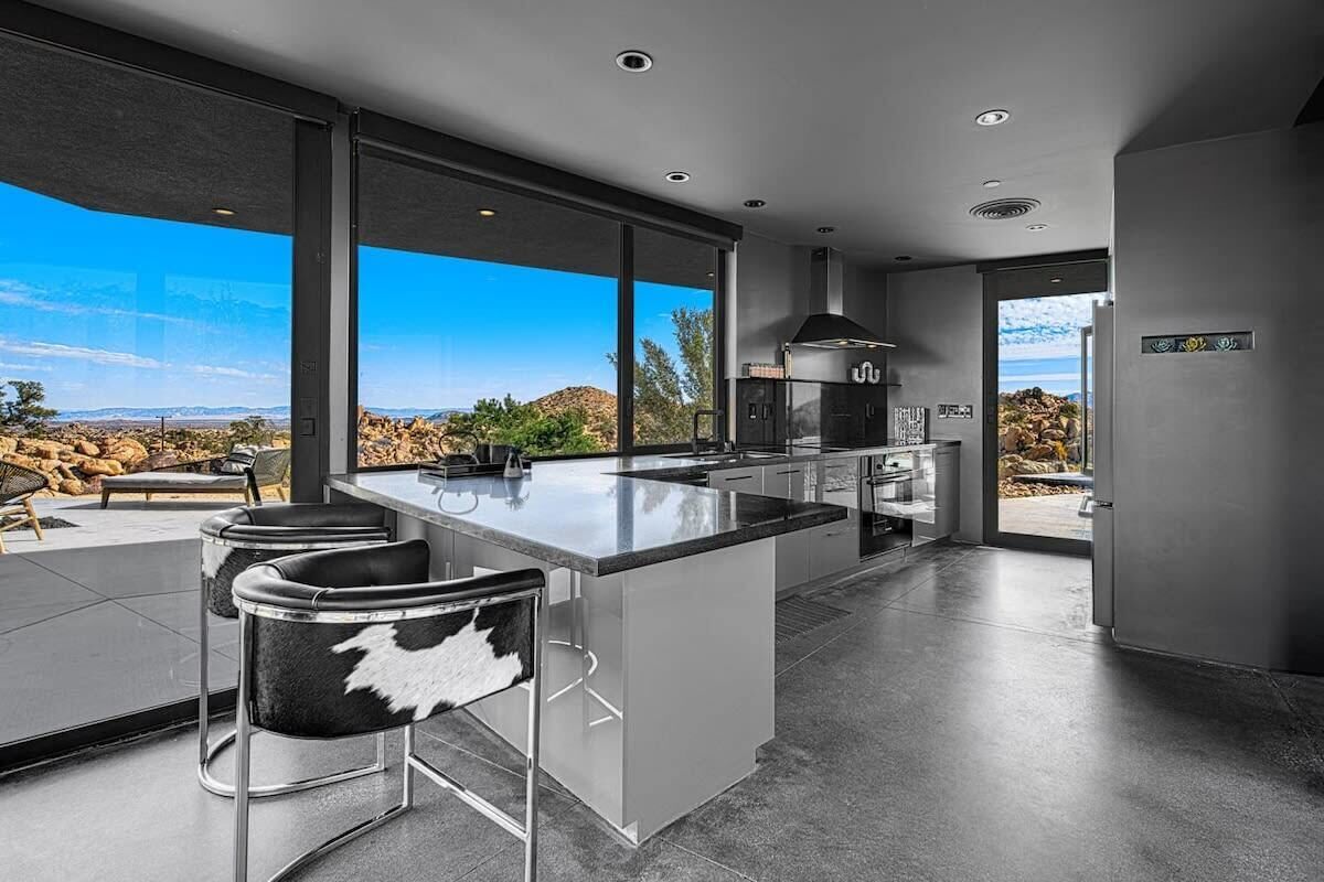 A modern kitchen with a large island, bar stools, and a view of the desert landscape.