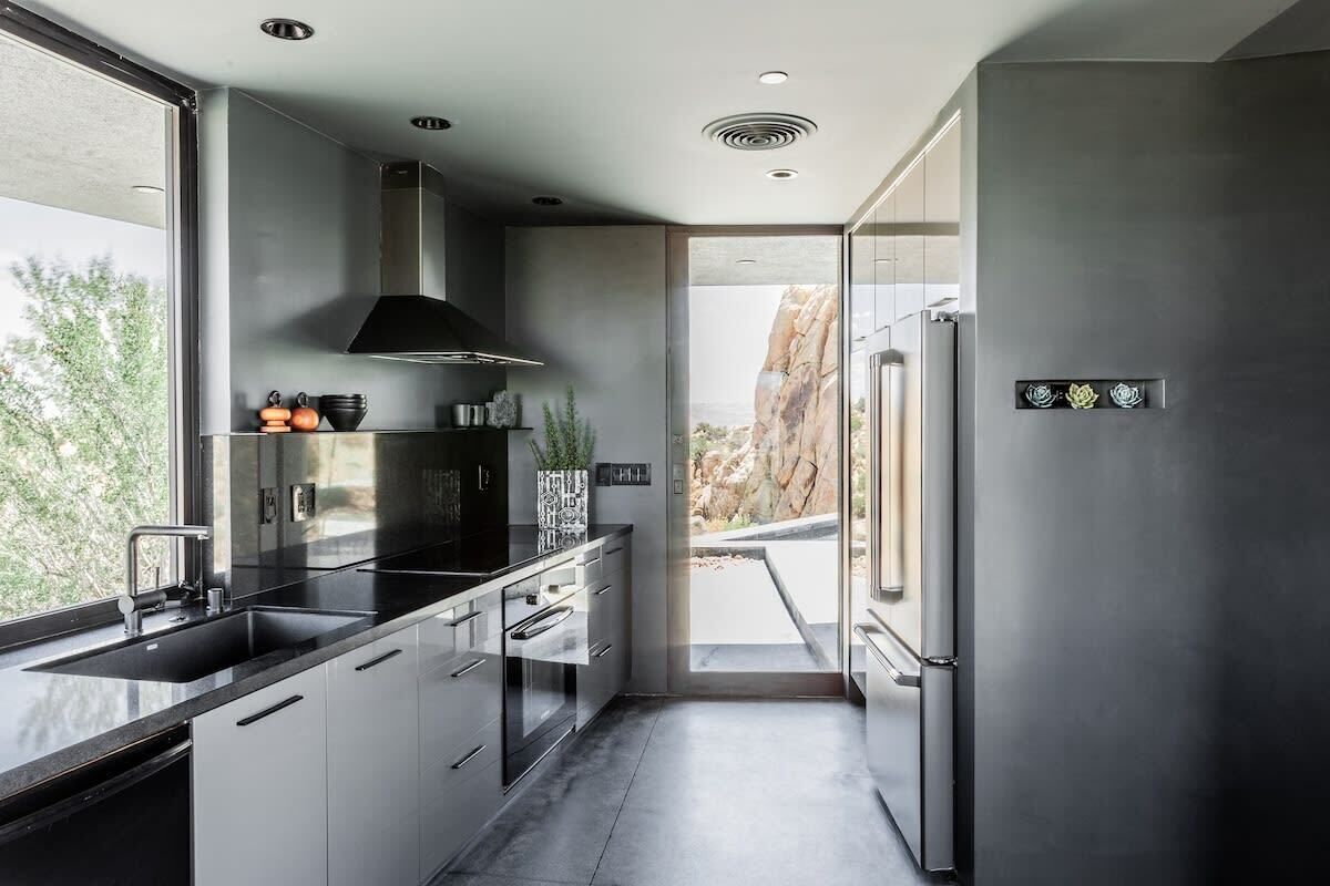 Une cuisine moderne avec un poêle noir, des appareils en acier inoxydable et une vue sur un paysage rocheux.