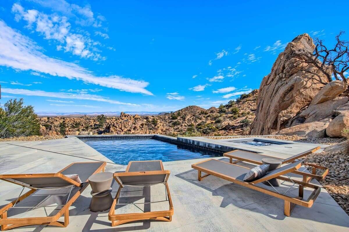 Ein Pool mit Liegestühlen und einem Whirlpool, umgeben von felsigem Gelände und blauem Himmel.