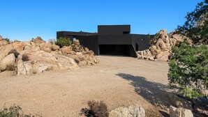 Un bâtiment moderne doté d’un toit plat, entouré de gros rochers et d’une végétation clairsemée.