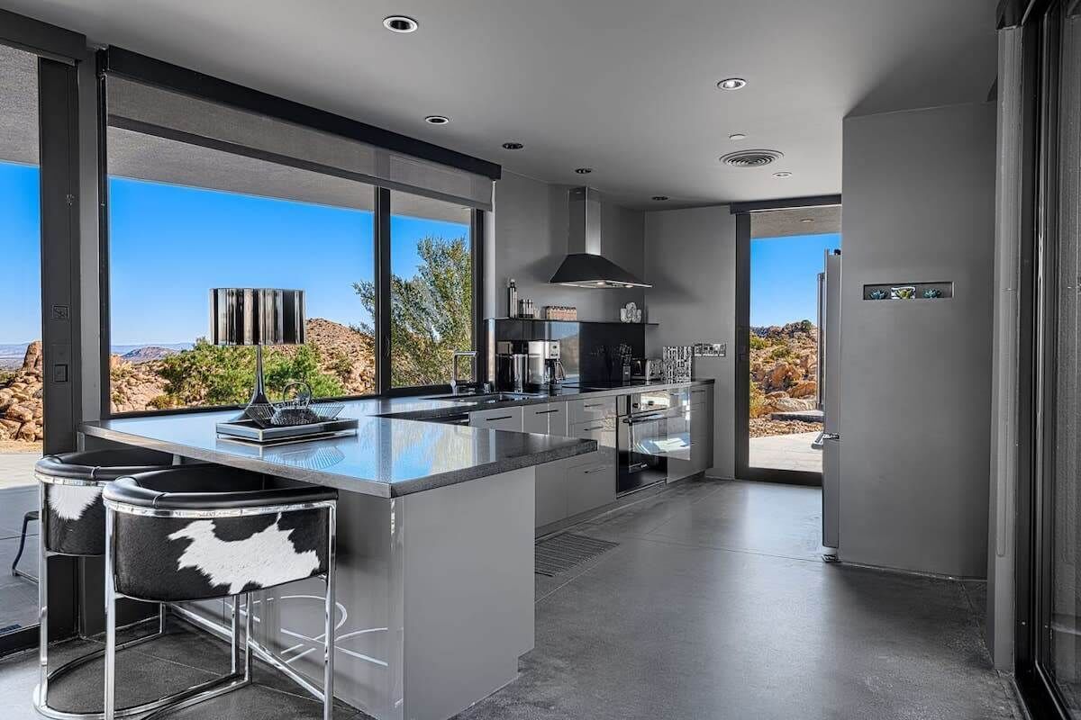 A modern kitchen with a large island, bar stools, and a view of the desert landscape.