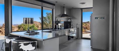 A modern kitchen with a large island, bar stools, and a view of the desert landscape.