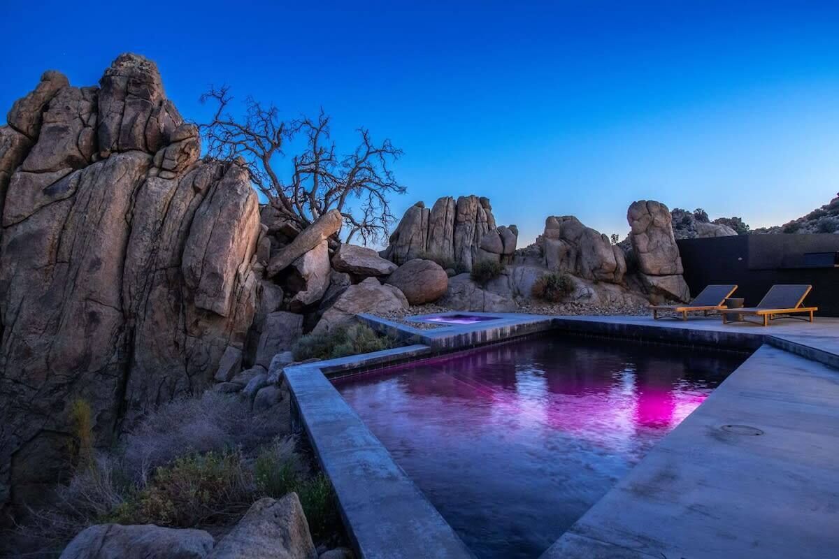 A pool with a stone border, surrounded by large rocks and a tree.