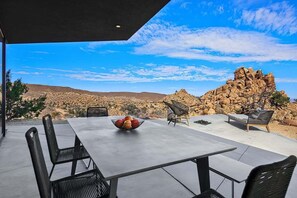 Une terrasse extérieure avec une table et des chaises, un saladier rempli de fruits et une vue sur un paysage rocheux.