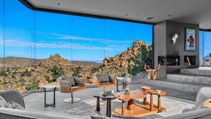 A modern living room with a large glass wall, a fireplace, and a view of rocky terrain. - Black Desert House ft in Architectural Digest (Yucca Valley)