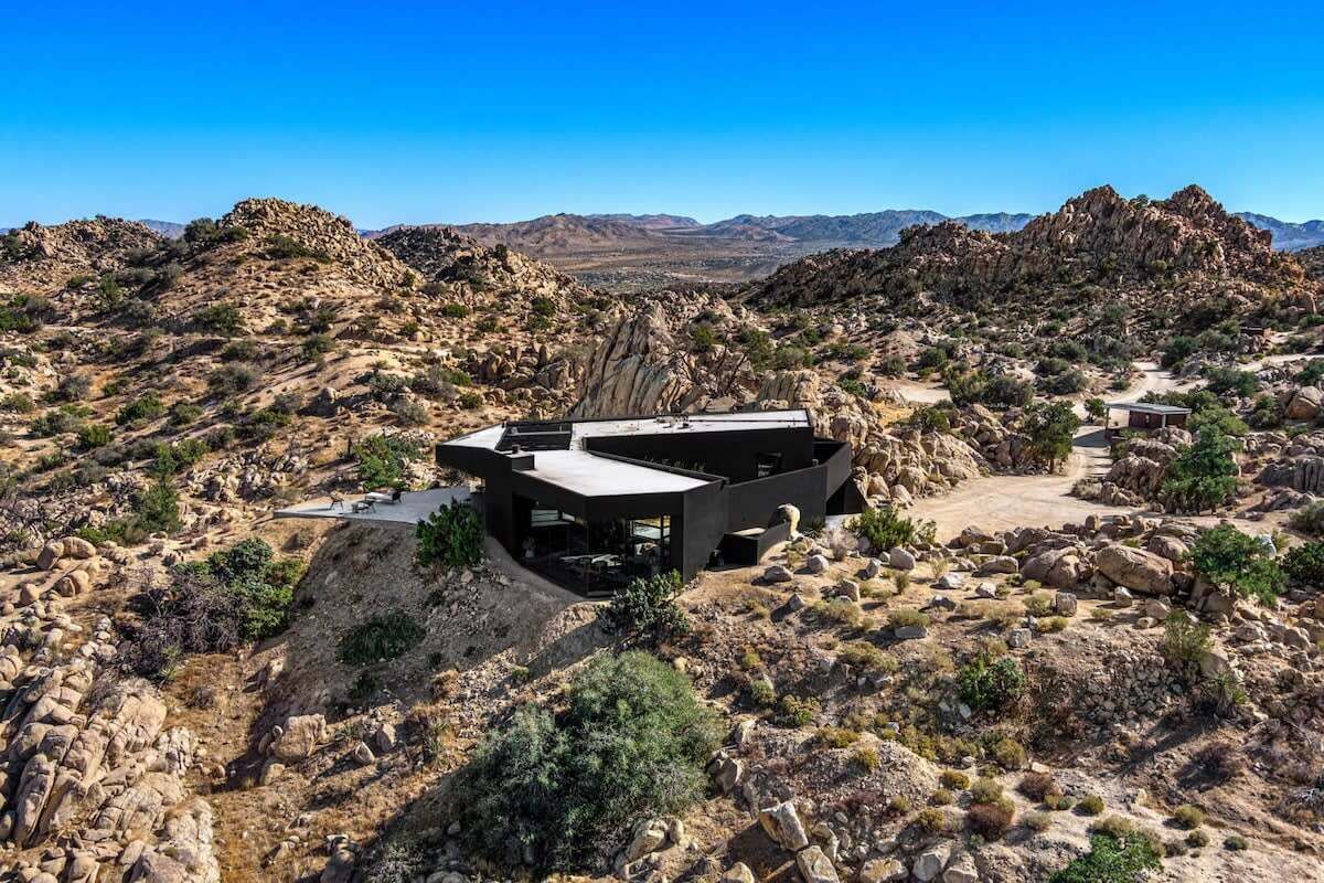 A modern building with a flat roof and large windows, surrounded by rocky terrain and sparse vegetation.