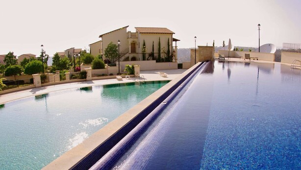 Una piscina de forma alargada, rodeada por un muro bajo y un edificio con tejado de baldosas.