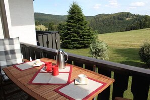 A wooden table with a metal coffee pot, two red cups, and two white cups on a balcony with a view of a forested hill. - Ferienwohnung Panorama Postwiese (Winterberg)