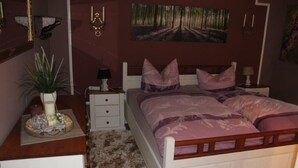 Ein Schlafzimmer mit Bett, Nachttischen, einer Wandlampe, einem Bild und einer Topfpflanze.