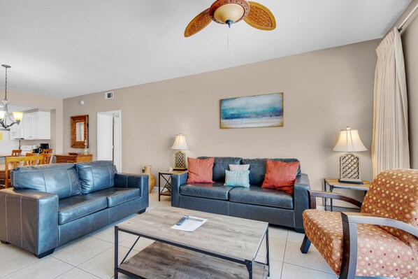 A living room with a sofa, coffee table, and armchairs. There is a dining area with chairs and a table.