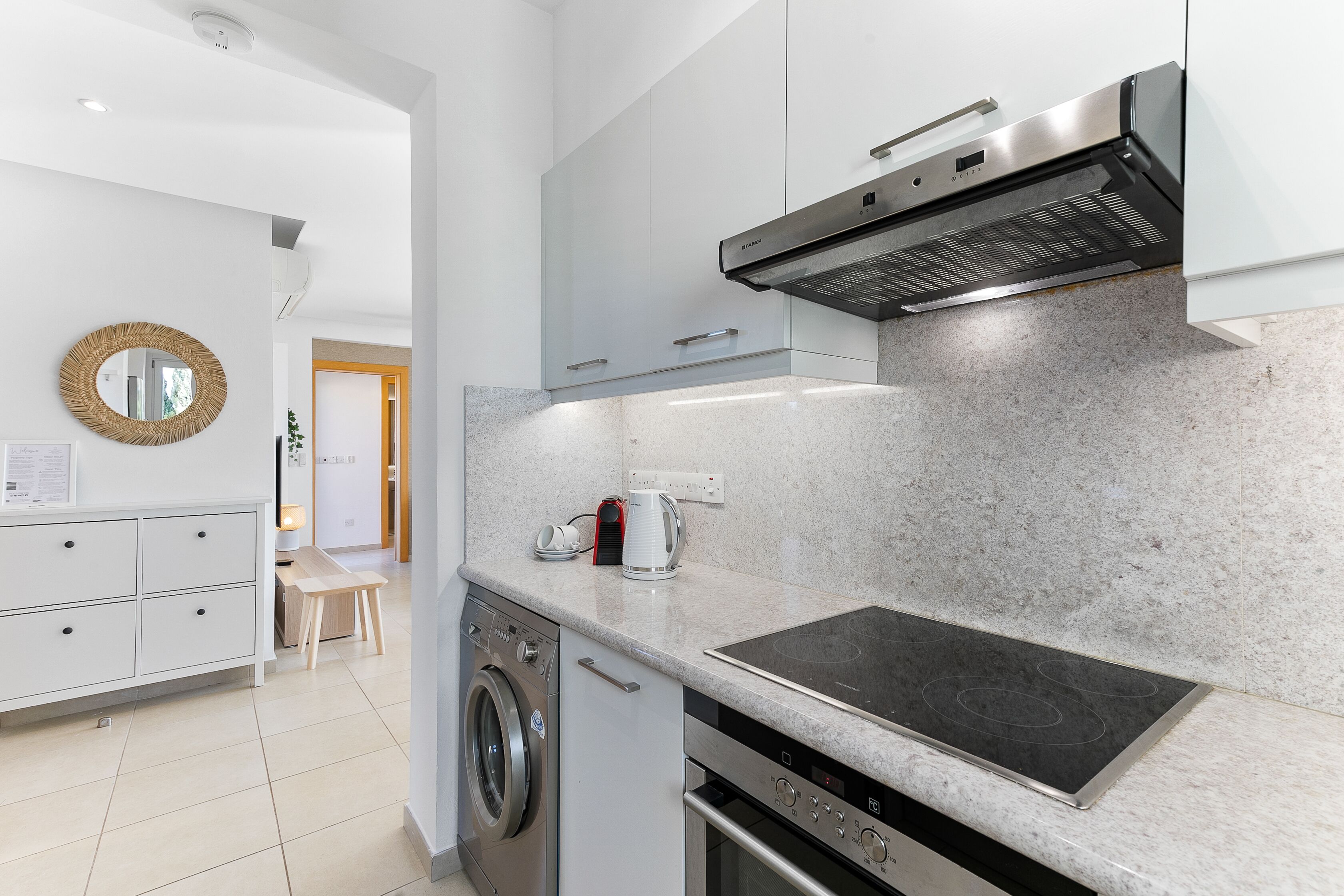 Une cuisine moderne équipée d’un four encastré, d’une plaque de cuisson et d’un lave-linge.