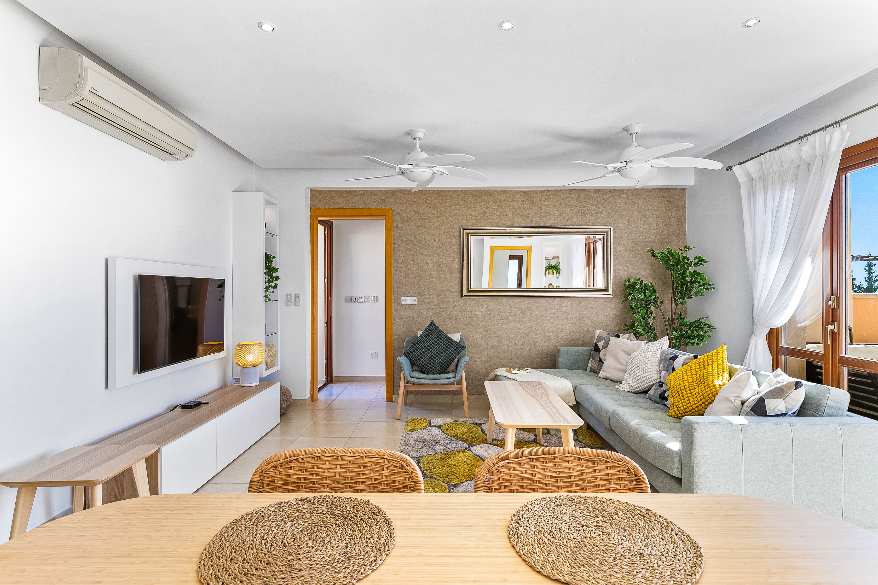 Una sala de estar moderna con sofá, televisor, ventiladores de techo y un comedor con mesa y sillas.