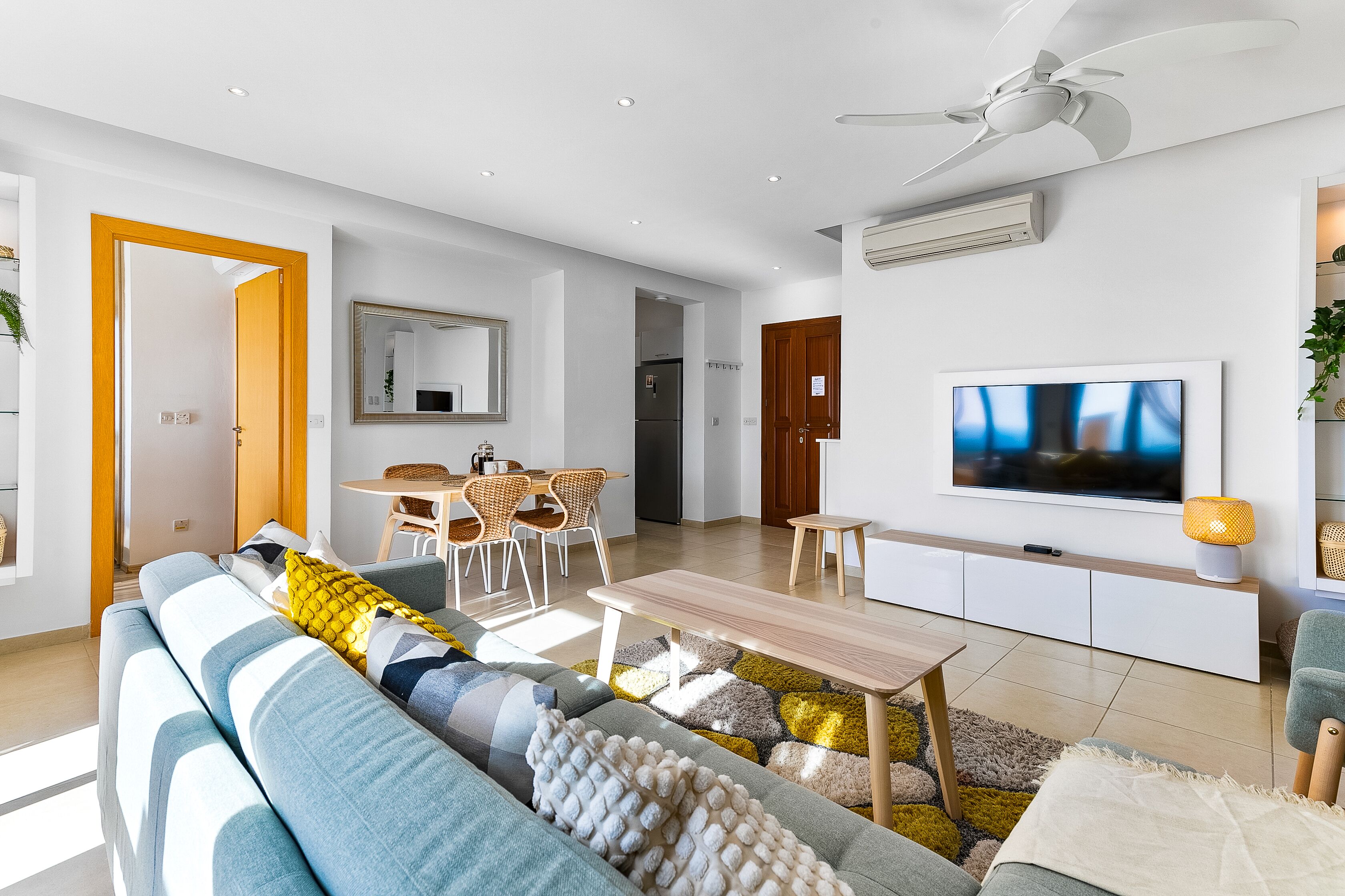A modern living room with a sofa, TV, dining area, and ceiling fan.