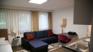 A hotel room with a sofa, a desk, a chair, a bed, a small table, a lamp, and a sink. - 1- Zimmer Apartment - Comfort Boardinghouse (Kornwestheim)