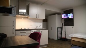 A compact room with a kitchenette, a dining area, a bed, and a TV mounted on the wall. - 1- Zimmer Apartment - Comfort Boardinghouse (Kornwestheim)