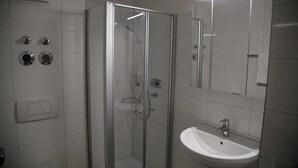 A bathroom with a glass-enclosed shower, a sink, and a mirror. - 1- Zimmer Apartment - Comfort Boardinghouse (Kornwestheim)
