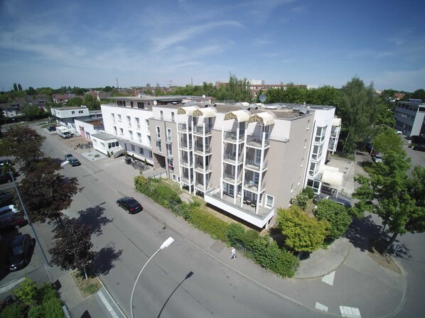 A multi-story building with balconies, a parking lot, and surrounding greenery.