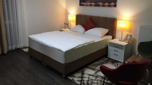A hotel room with a bed, two bedside tables, a chair, a painting, and a radiator. - 3- Zimmer Apartment - Comfort Boardinghouse (Kornwestheim)