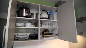 A kitchen cabinet with shelves containing cookware, pots, pans, and utensils. - 3- Zimmer Apartment - Comfort Boardinghouse (Kornwestheim)
