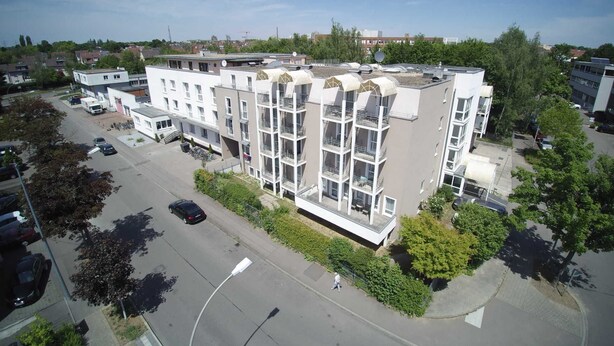 A multi-story building with balconies, a parking lot, and surrounding greenery. - 3- Zimmer Apartment - Comfort Boardinghouse (Kornwestheim)