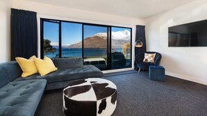 A modern living room with a large window offering a view of a lake and mountains.