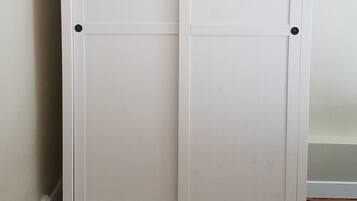 A white wardrobe with two doors and a flat top shelf, placed against a wall with a wooden floor.