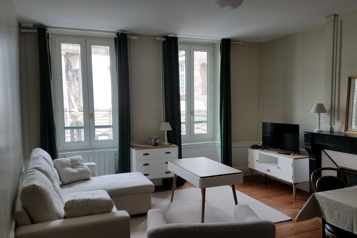 A modern hotel room with a sofa, a small table, a TV, and a fireplace.